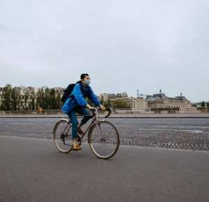 Man wearing denim riding a bike on an empty paris street, with a covid mask