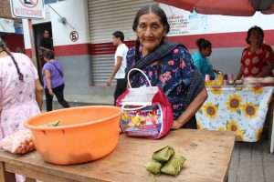 Old woman in Oaxaca, Mexico buying groceries on the street with diverse people walking around.